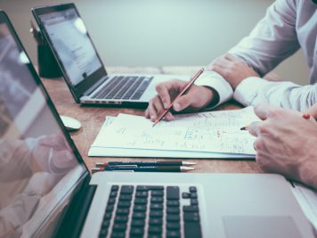 person holding pencil with paper and laptops
