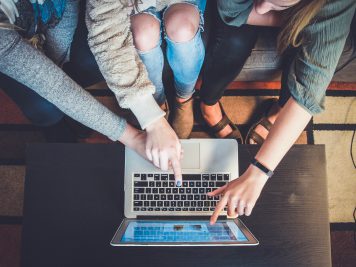 Three people pointing at a silver laptop