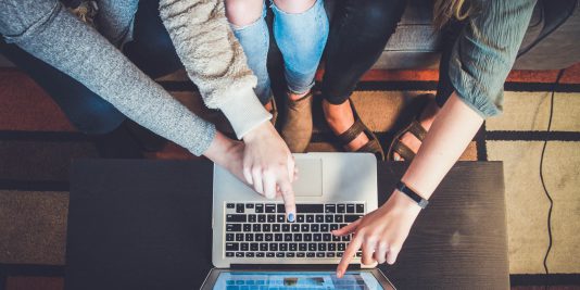 Three people pointing at a silver laptop