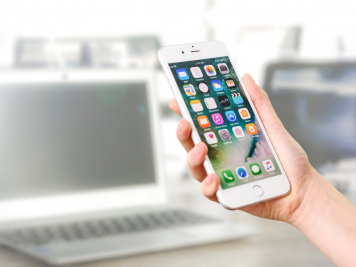 Person holding iPhone in front of laptop