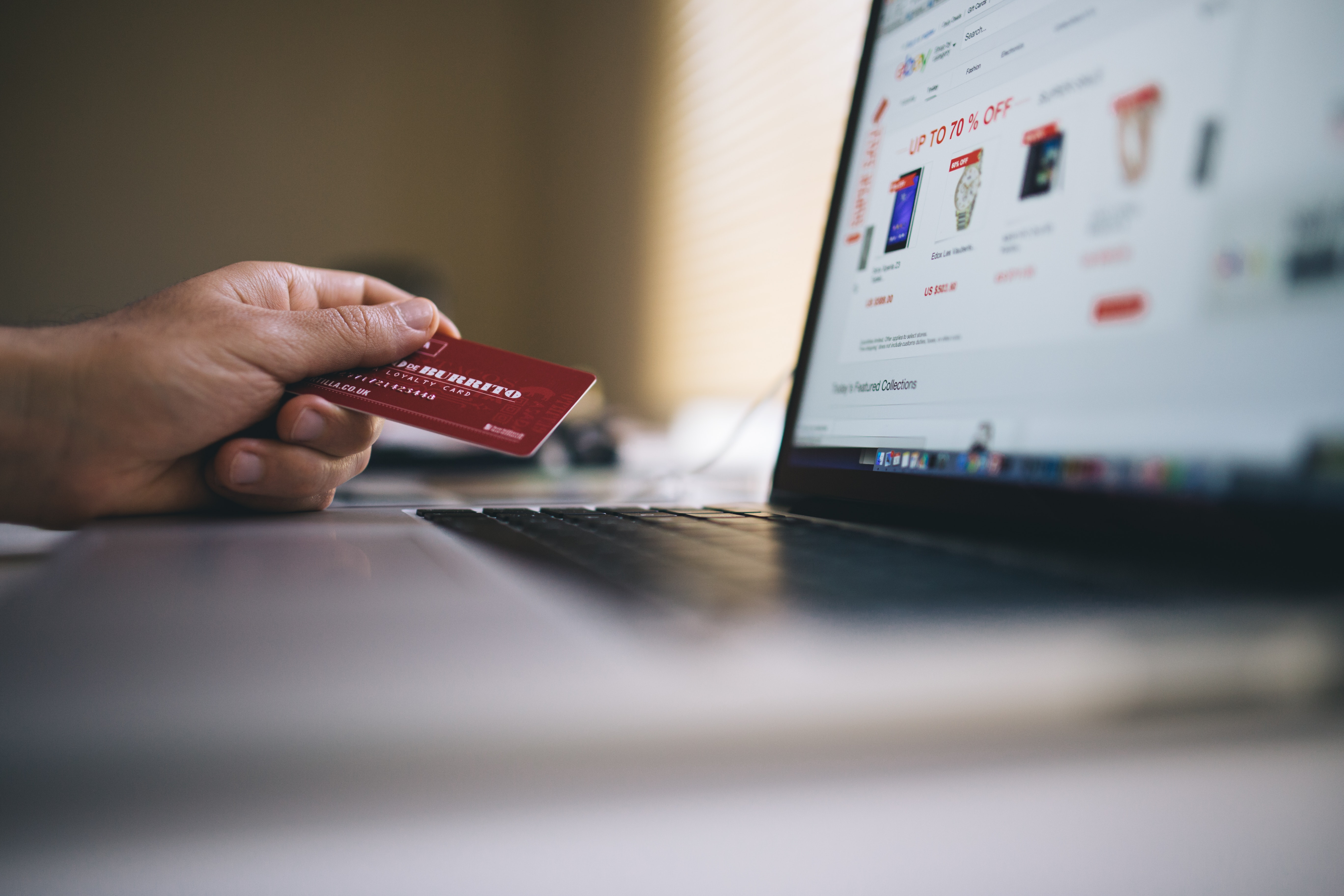 hand holding a credit card in front of a computer